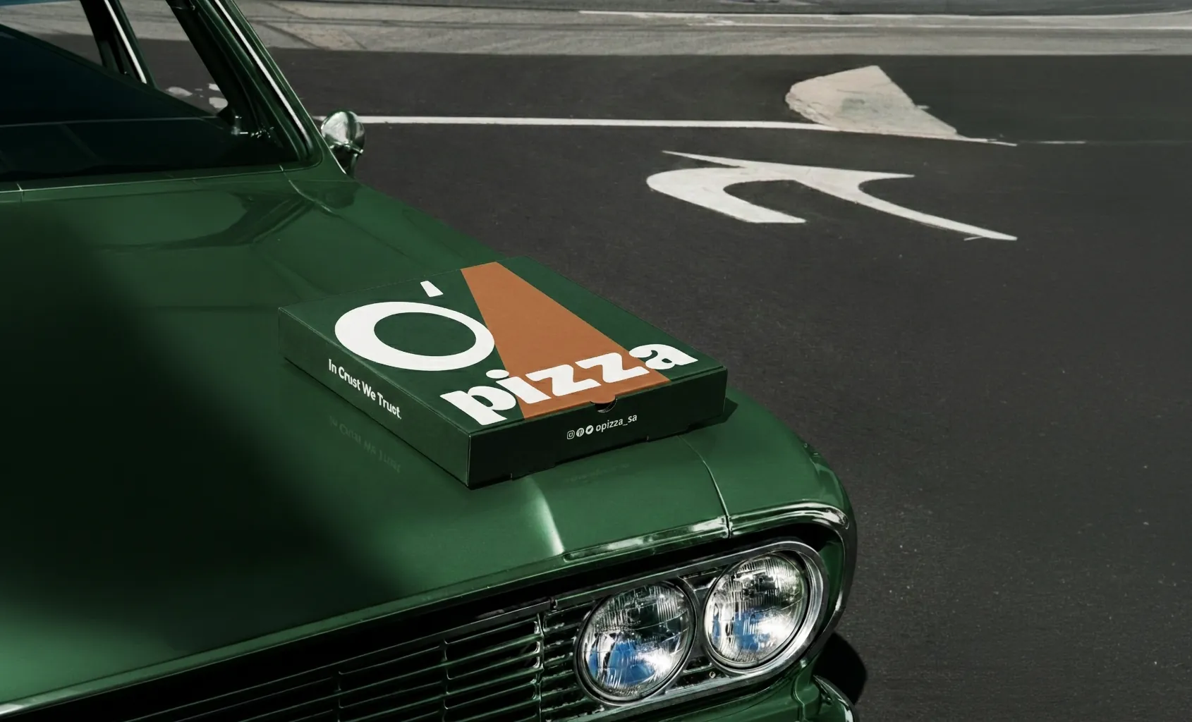 علبة بيتزا O’Pizza بشعار In Crust We Trust على سيارة خضراء